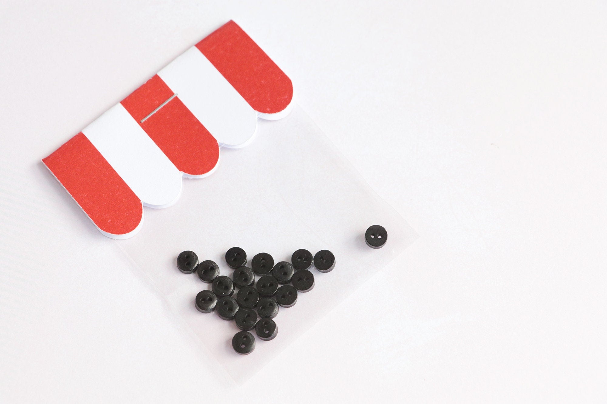 twenty small black buttons in red and white packaging